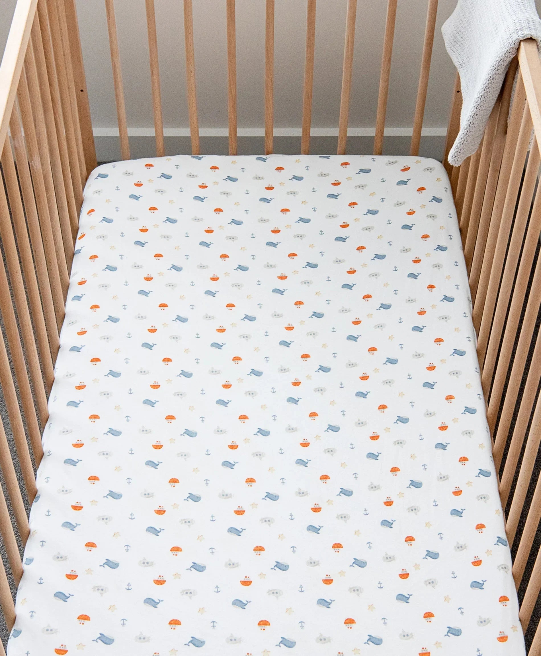 Clean fitted cot sheet on a wooden baby cot mattress, viewed from above.