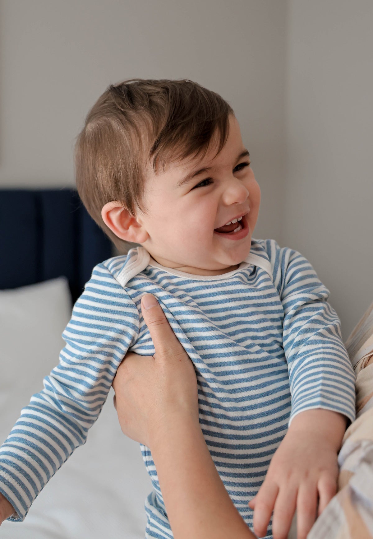 Smiling baby in a blue and white striped Lūmmi in Colour cotton onesie being held by a parent