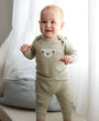 Organic Cotton Long Sleeve Bodysuit - Chenille Koala Bear baby standing with a cheerful expression while wearing a chenille koala bear long sleeve bodysuit, for parents seeking soft babywear.